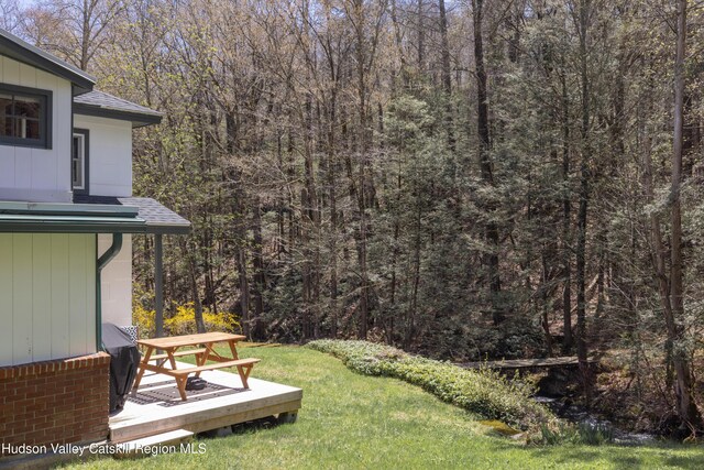 view of green lawn featuring a forest view