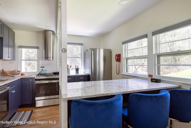 kitchen featuring stainless steel appliances, range hood, light stone counters, light wood-type flooring, and tasteful backsplash