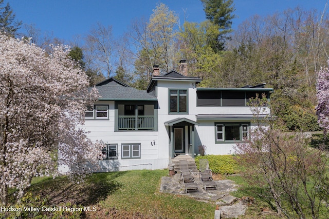 view of front of property with a chimney, roof with shingles, a balcony, and a front yard