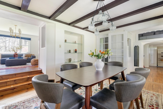 dining space with a chandelier, hardwood / wood-style floors, beamed ceiling, built in shelves, and arched walkways