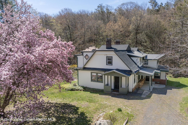 view of front of property with a chimney, a front yard, and a shingled roof