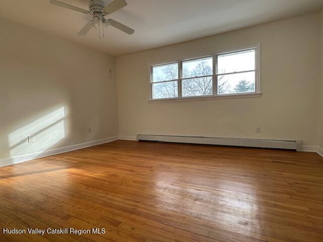 empty room with baseboard heating, light wood-type flooring, and ceiling fan