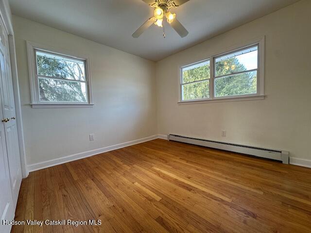 empty room with ceiling fan, a healthy amount of sunlight, a baseboard heating unit, and light hardwood / wood-style floors