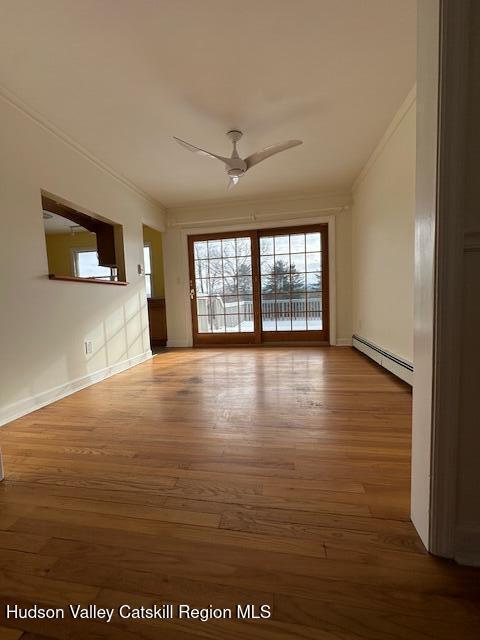 unfurnished room with baseboard heating, crown molding, wood-type flooring, and ceiling fan