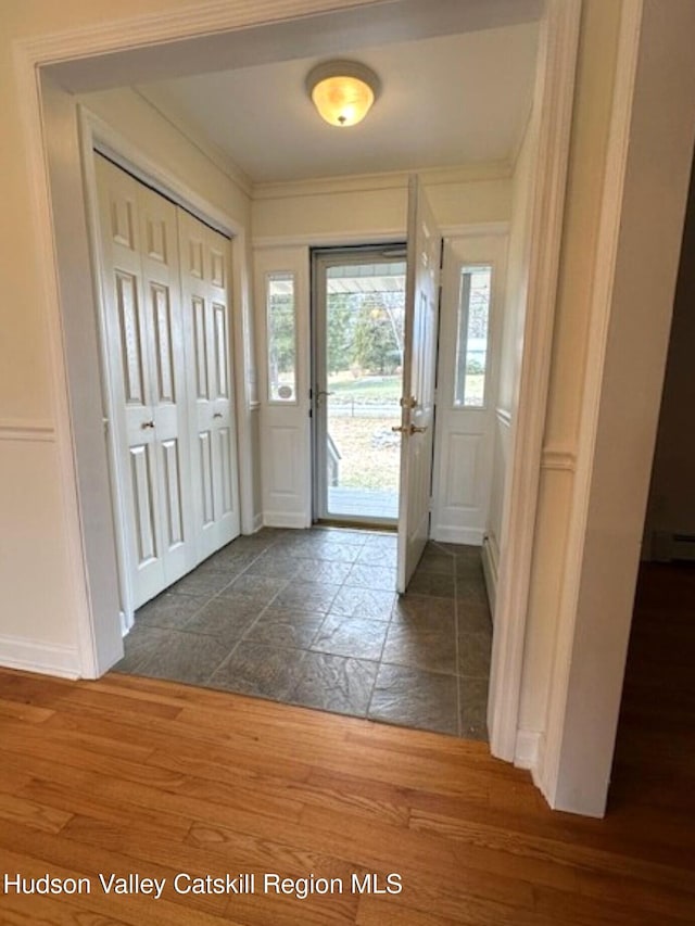 foyer entrance with baseboard heating and crown molding