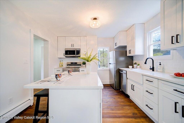 kitchen with a kitchen bar, white cabinetry, a baseboard heating unit, a sink, and appliances with stainless steel finishes