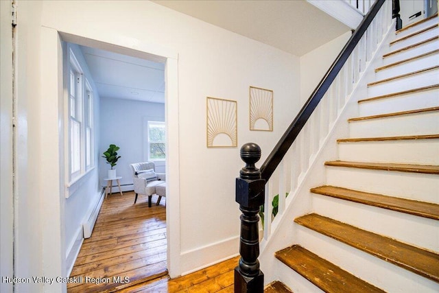 stairs with baseboards, a baseboard heating unit, and hardwood / wood-style flooring