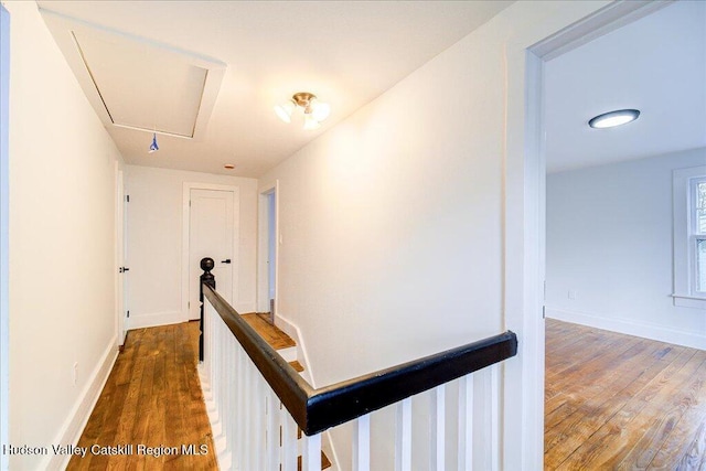 hallway featuring baseboards, an upstairs landing, wood finished floors, and attic access