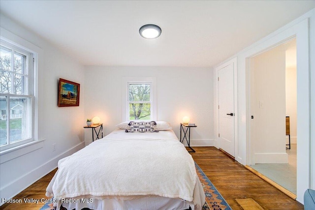 bedroom with baseboards, multiple windows, and dark wood-type flooring
