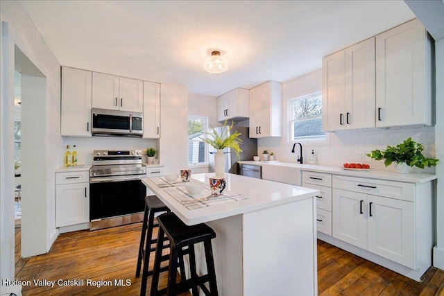 kitchen with a healthy amount of sunlight, a kitchen breakfast bar, stainless steel appliances, and dark wood-style flooring