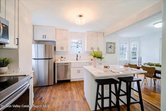 kitchen featuring a breakfast bar, light countertops, a sink, dark wood finished floors, and appliances with stainless steel finishes