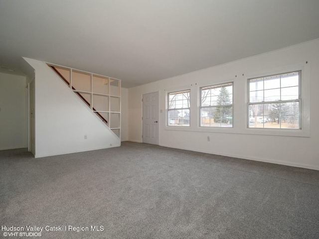 unfurnished living room with a wealth of natural light, carpet, and stairway