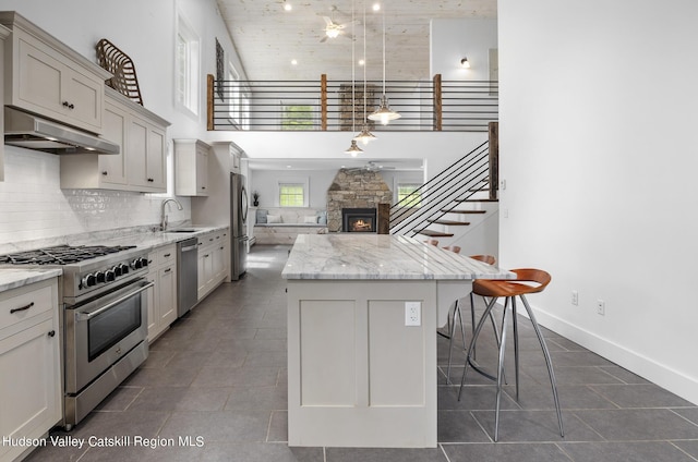 kitchen with sink, stainless steel appliances, light stone counters, a kitchen island, and decorative light fixtures