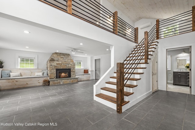 staircase with a high ceiling, a stone fireplace, a wealth of natural light, and ceiling fan