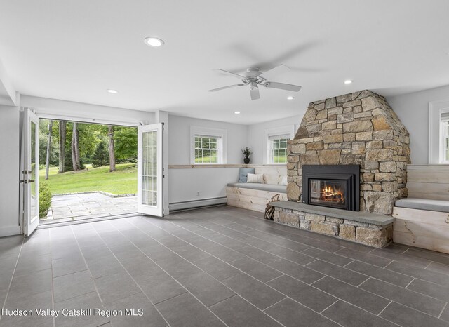 unfurnished living room featuring ceiling fan, a baseboard radiator, a stone fireplace, and tile patterned flooring