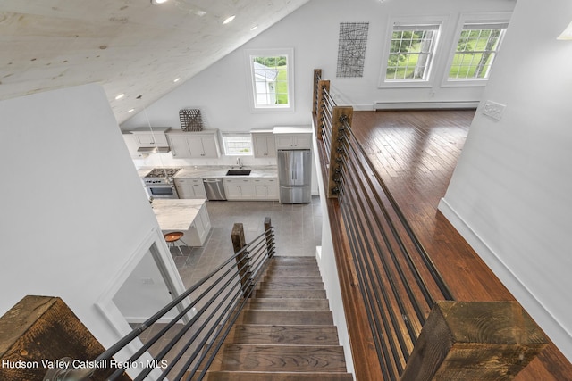 stairway with baseboard heating, plenty of natural light, sink, and hardwood / wood-style floors