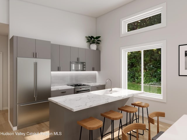 kitchen with a kitchen bar, appliances with stainless steel finishes, gray cabinetry, sink, and light hardwood / wood-style floors