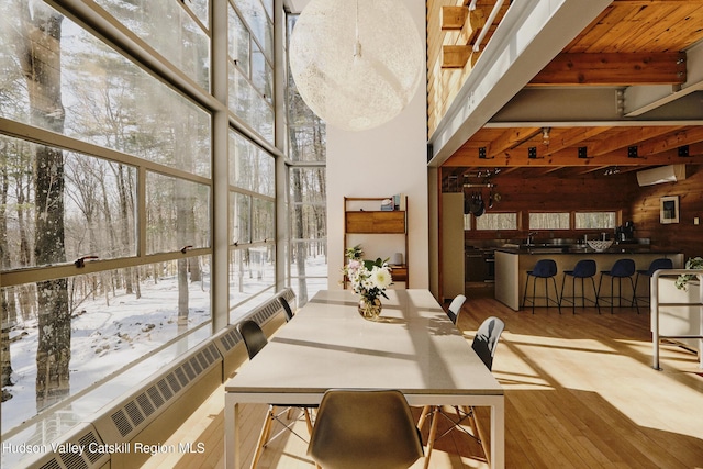 dining room featuring a healthy amount of sunlight, a wall mounted AC, light hardwood / wood-style floors, and a high ceiling