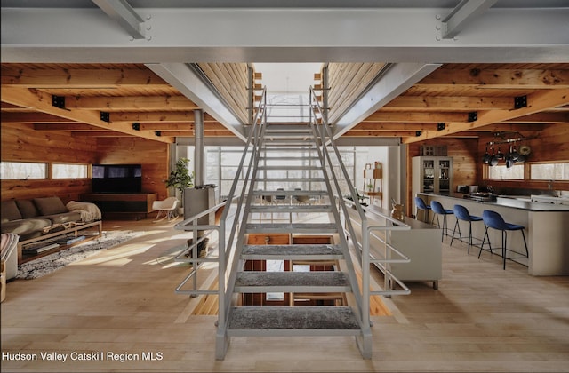 stairway featuring beam ceiling, wooden walls, wood-type flooring, and plenty of natural light