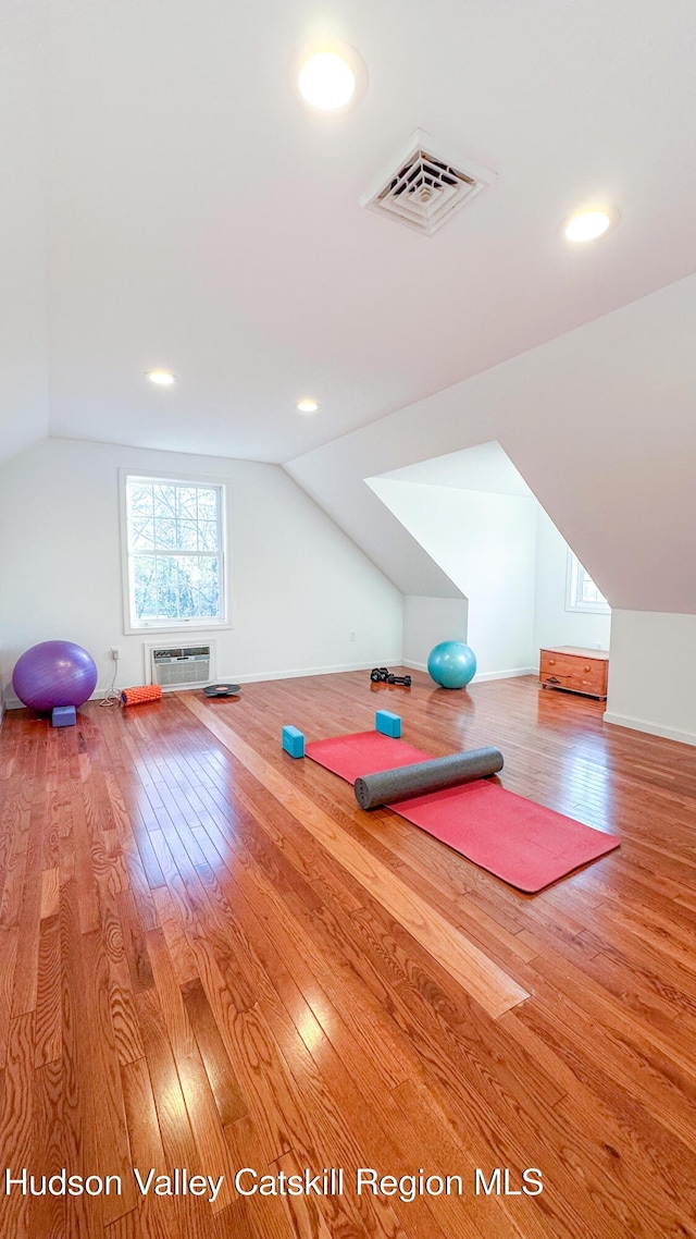exercise room with a wall unit AC, lofted ceiling, wood finished floors, and visible vents