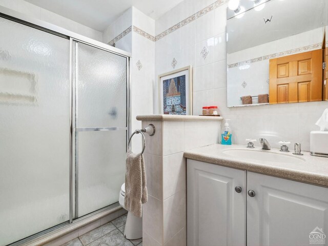 full bath with tile walls, a stall shower, vanity, and tile patterned floors