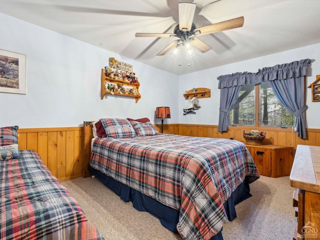 bedroom featuring wainscoting, wood walls, carpet floors, and a ceiling fan