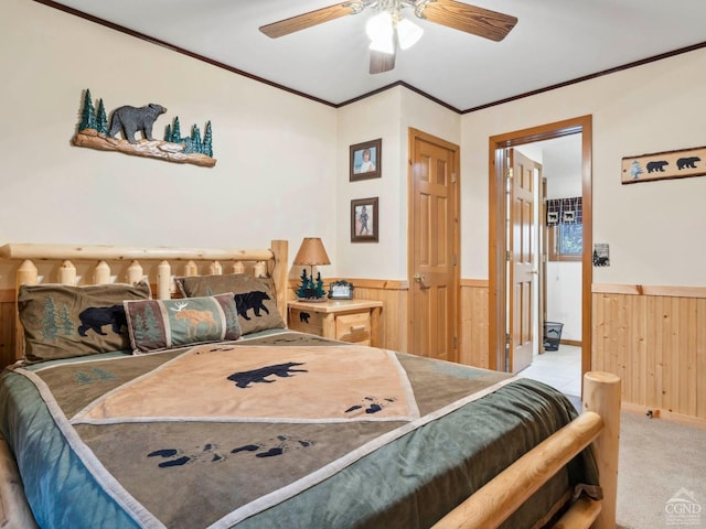 carpeted bedroom with a wainscoted wall, wood walls, ornamental molding, and a ceiling fan