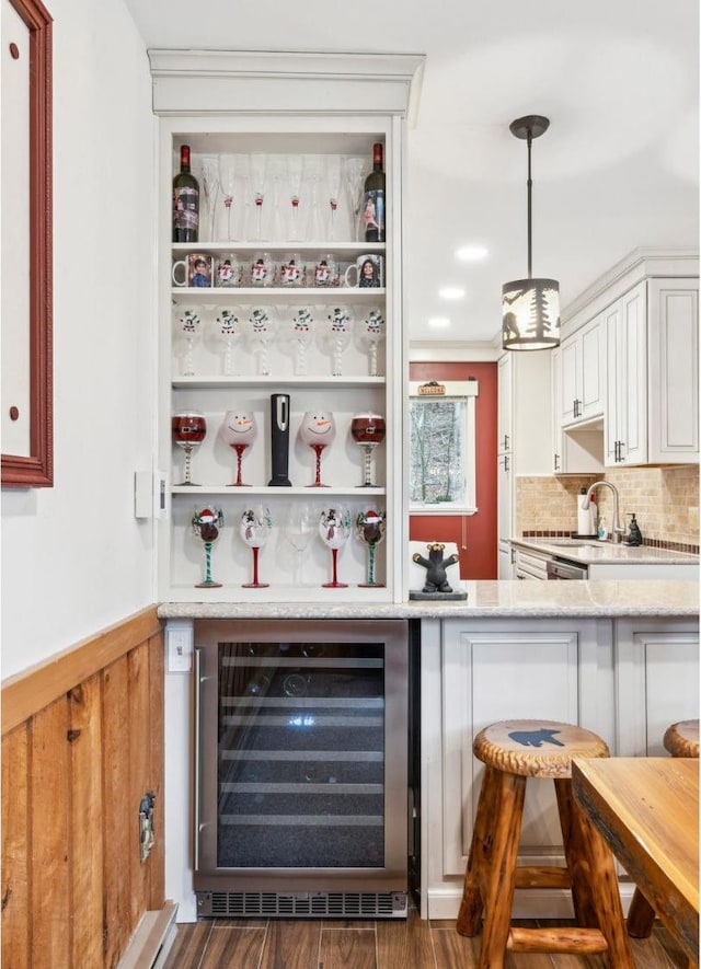 indoor dry bar featuring wine cooler, backsplash, dark wood-style floors, hanging light fixtures, and wainscoting