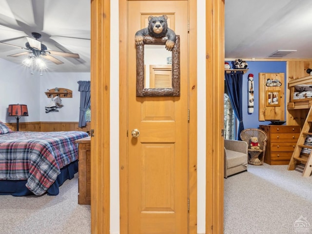bedroom with carpet floors, wooden walls, and a wainscoted wall
