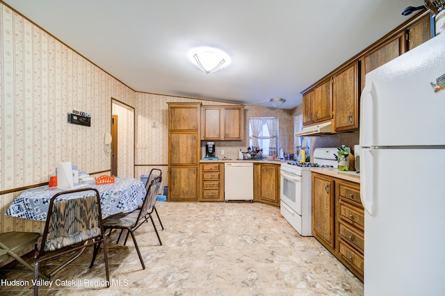 kitchen featuring wallpapered walls, under cabinet range hood, light countertops, brown cabinets, and white appliances