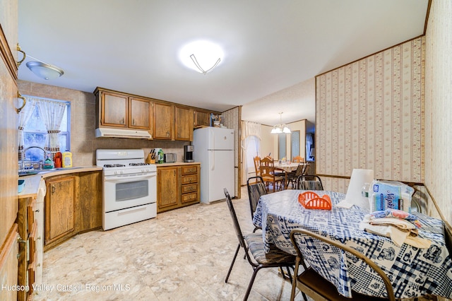 kitchen with white appliances, brown cabinetry, wallpapered walls, light countertops, and under cabinet range hood