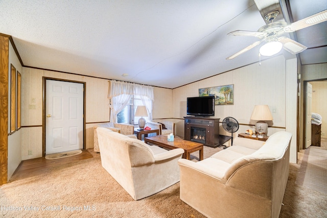 carpeted living area featuring a ceiling fan, vaulted ceiling, a textured ceiling, a glass covered fireplace, and crown molding