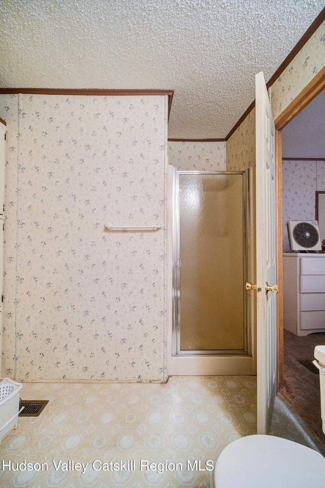 full bathroom featuring wallpapered walls, a stall shower, ornamental molding, a textured ceiling, and toilet