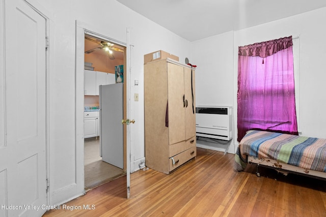 bedroom featuring heating unit, white fridge, and light hardwood / wood-style flooring