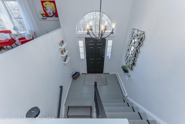 foyer entrance with a chandelier, a towering ceiling, baseboard heating, and plenty of natural light