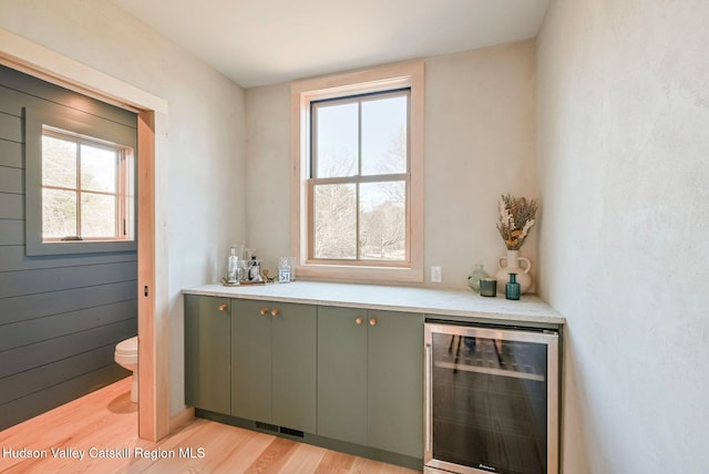 bar featuring beverage cooler, green cabinets, and light wood-type flooring