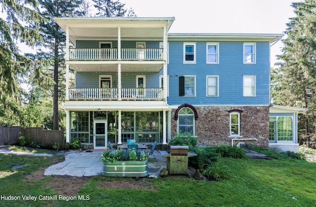 rear view of house with a balcony, a yard, and a patio