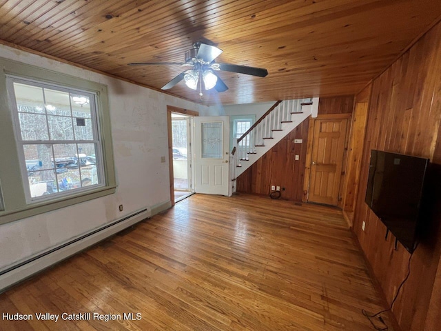 unfurnished living room featuring wood ceiling, ceiling fan, a baseboard heating unit, light hardwood / wood-style flooring, and wood walls