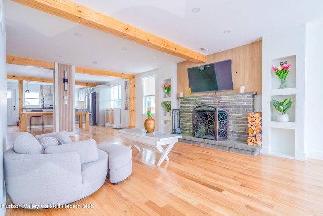 living room with hardwood / wood-style floors, built in shelves, beam ceiling, and a brick fireplace