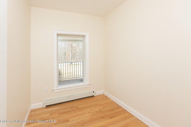 spare room featuring light wood finished floors, a baseboard heating unit, and baseboards