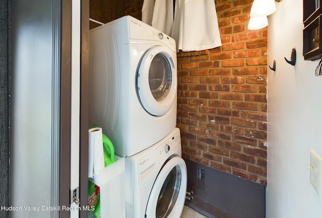 laundry room with brick wall and stacked washer and dryer