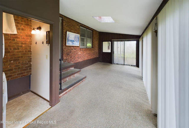 hall featuring light colored carpet, vaulted ceiling, and brick wall