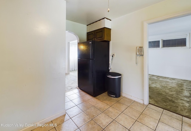 kitchen featuring dark brown cabinetry, black fridge, and light carpet