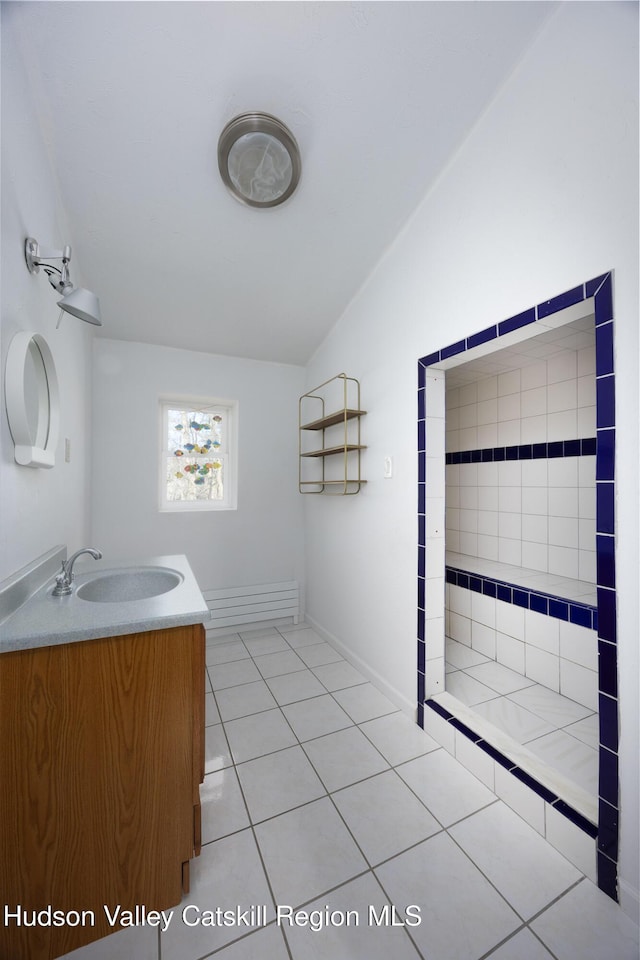 full bathroom featuring a tile shower, tile patterned flooring, vanity, baseboards, and lofted ceiling