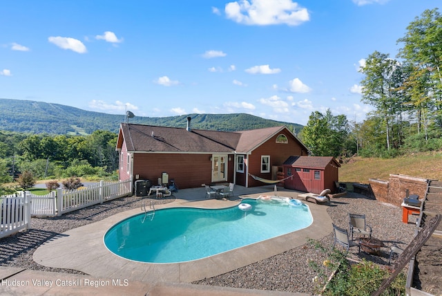 view of pool featuring a mountain view, a patio, an outdoor fire pit, and a storage shed