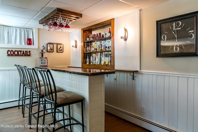 bar with a dry bar, wood finished floors, baseboard heating, and wainscoting