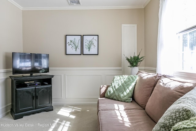 living area with visible vents, crown molding, light carpet, wainscoting, and a decorative wall