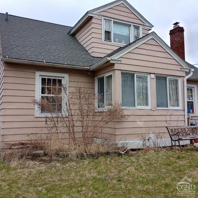 view of side of property with a shingled roof, a chimney, and a yard