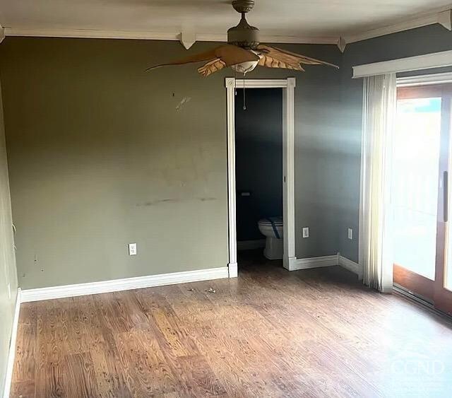 empty room with ornamental molding, a ceiling fan, wood finished floors, and baseboards