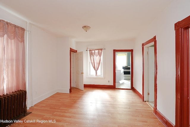 spare room featuring light wood-style floors, radiator, and baseboards